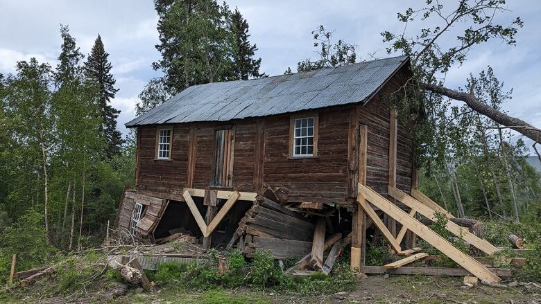 A log cabin building with a tree that fell on top of it. 