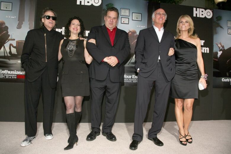 Five people in fancy attire pose in front of a photowall. 