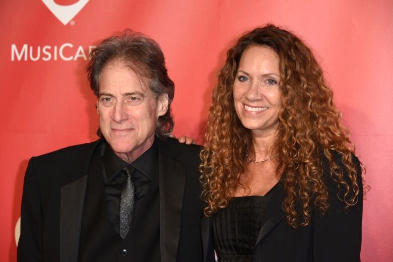 A man and woman pose in front of a red wall. 