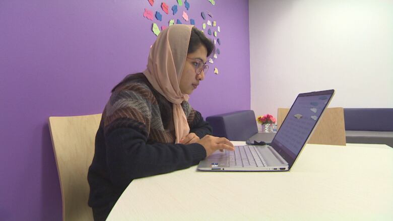 A woman sits at a table using a laptop