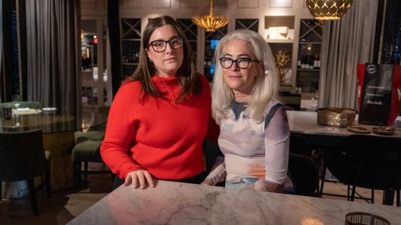 Two women pose at a table in a dimly lit restaurant.