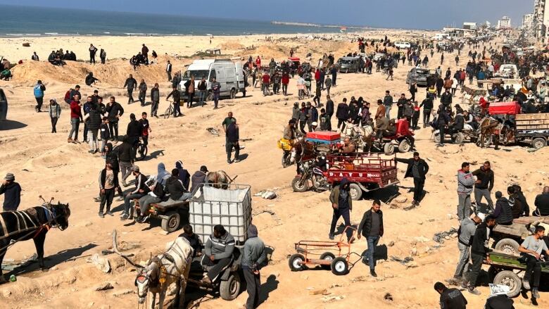 Hundreds of people gather on a beach with carts and other vehicles to collect humanitarian aid.