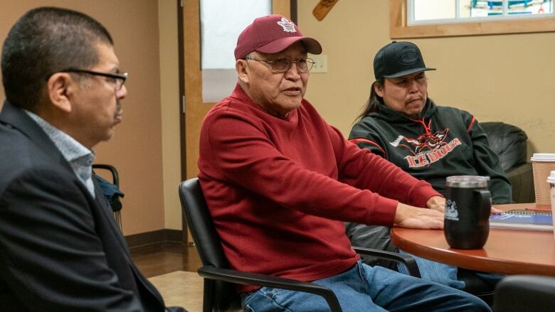 Three people sit inside around a table.