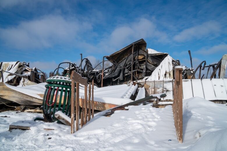 A large, burnt structure covered in snow is seen beneath a bright blue sky.