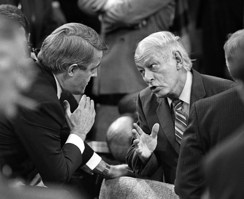 Two men speak in a crowded room.