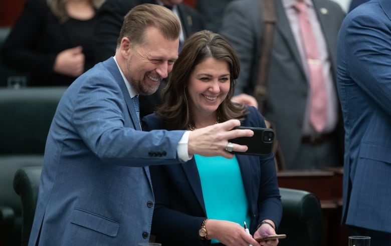 Two people in suits smile as they take a photo.