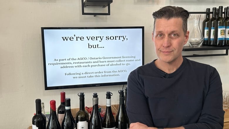 Dan Grant stands in front of a screen that says 'we're sorry but...' alongised bottles of wine for sale.  