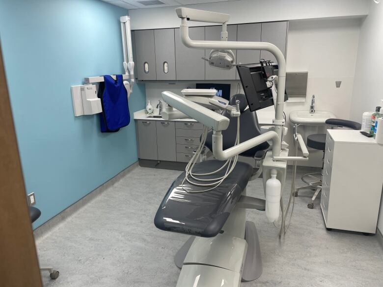 A dental chair is empty in a brightly lit white clinical room.