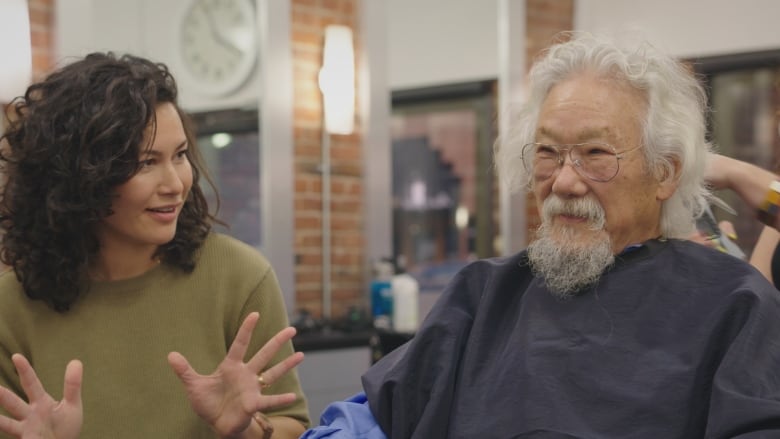 A woman with shoulder-length wavy brown hair sits next to a man with white hair and a grey goatee. 