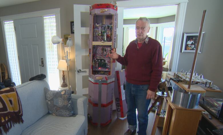 A man stands next to a six foot tall contraption with wires and computers inside.