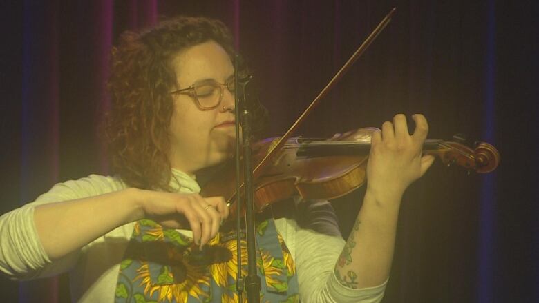 A woman with curly hair and glasses plays a violin. 