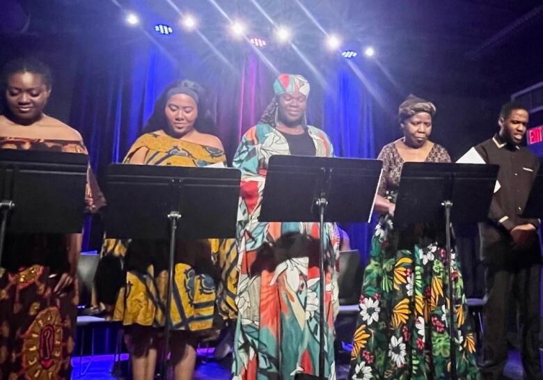 Picture of five people standing on a stage, reading from raised music stands. 