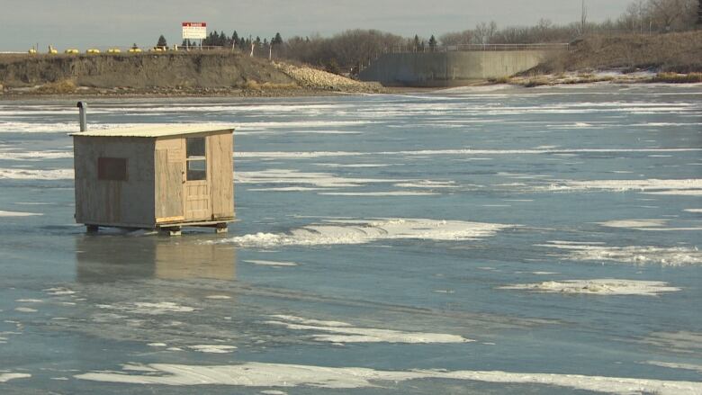 An ice shack sits on a frozen and slushy lake.