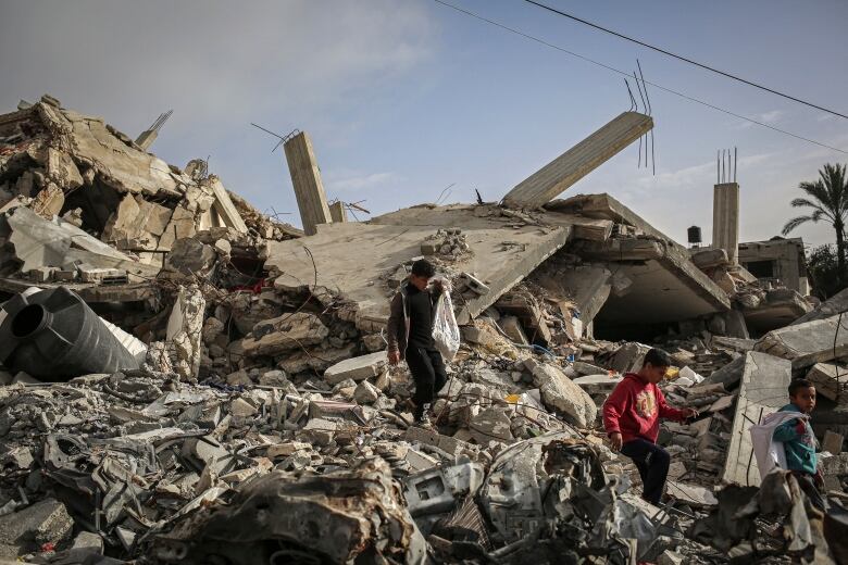 Children carry their belongings as they navigate over the rubble of a destroyed building.