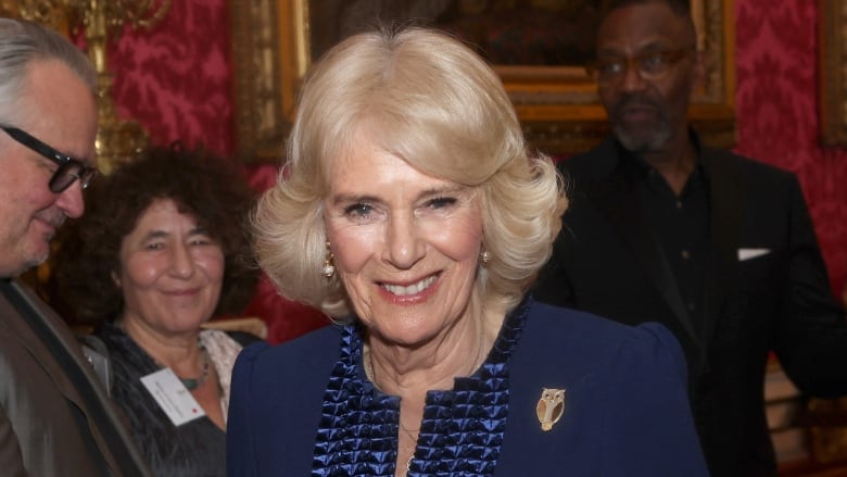 An older woman in a blue gown smiles at  the camera