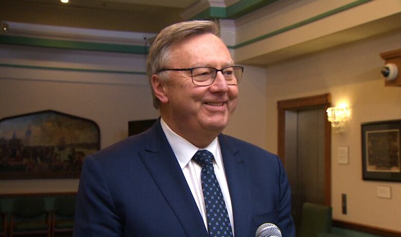 A man in a blue suit standing behind a microphone in a lobby. 