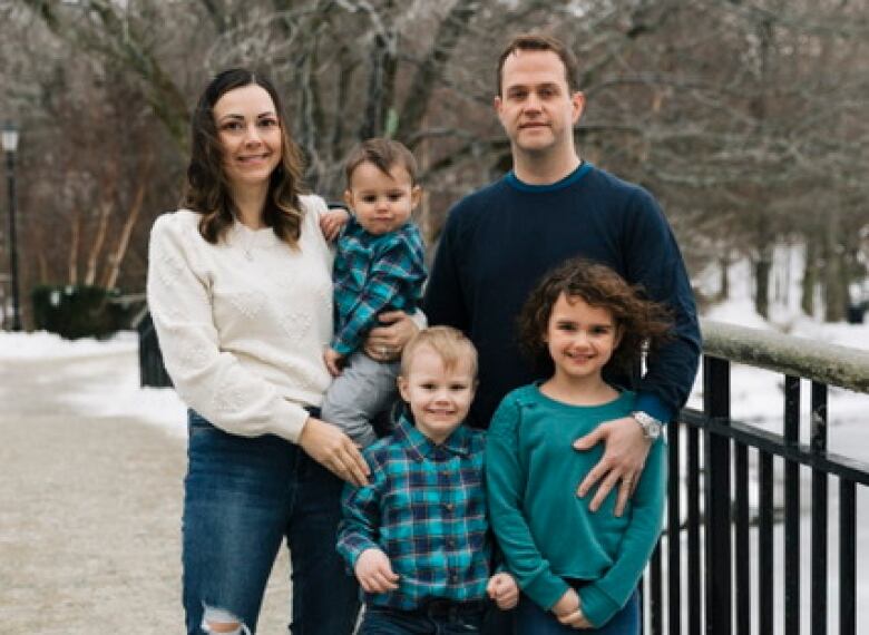 A woman stands, smiling, with three young kids and a man on a snow-covered bridge.