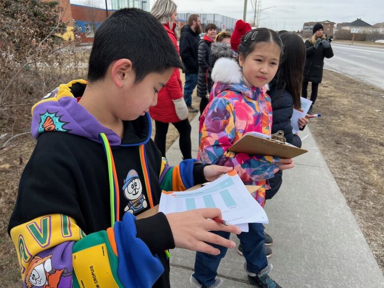 Elementary school children stand on the sidewalk in front of their school to observe traffic