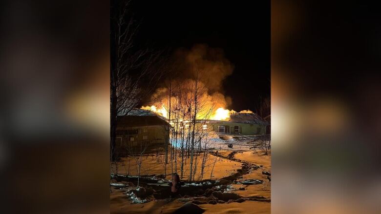 A building is seen on fire at night, surrounded by snow-covered ground and a smoky sky.