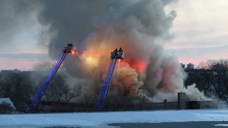 Firefighters direct water from two ladders, down onto the roof of a building on fire.