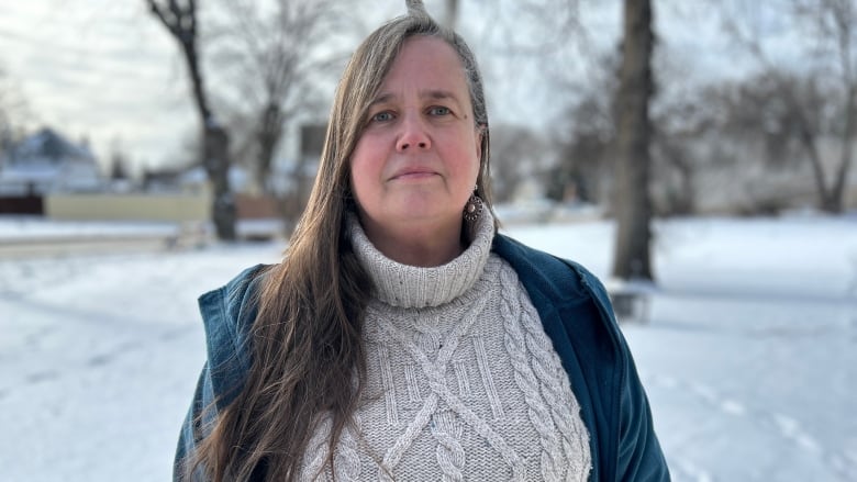 A woman with long hair over her right shoulder is pictured in a snowy scene wearing a blue unzipped jacket over a grey turtleneck wool sweater.