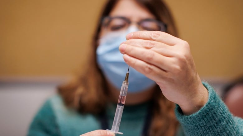 A woman in a mask prepares a syringe