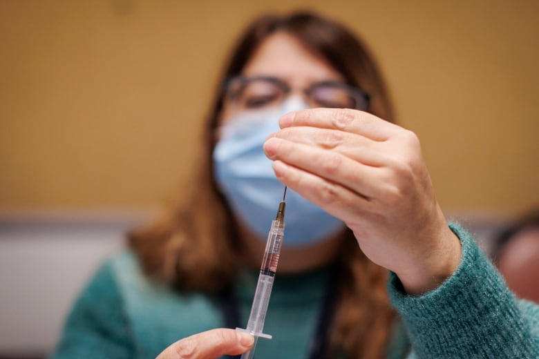 A woman in a mask prepares a syringe