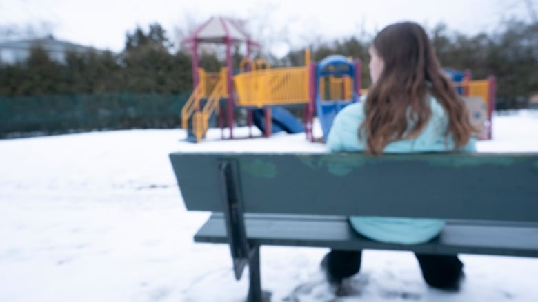 Blurred shot of young teen with long hair sitting on bench in playground.