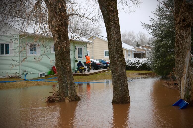 A flooded back yard with people in hi-vis gear pumping water. 