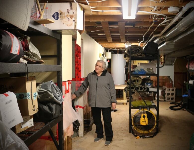 A white-haired woman shows off flood-proofing measures in her basement. 