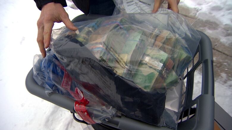 A laundry basket contains a plastic bag full of cash.