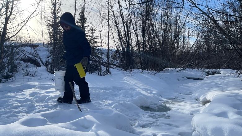 A woman in a parka carries a pail full of water away from a nearby creek, which many near Mendenhall use for their drinking water.