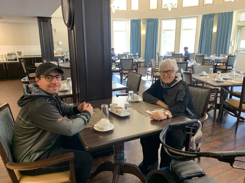 A  young man and older woman smile while posing for a photo in a dining room with many tables.