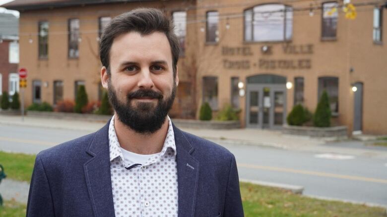 A man smiles at the camera, standing outside a city hall building. 