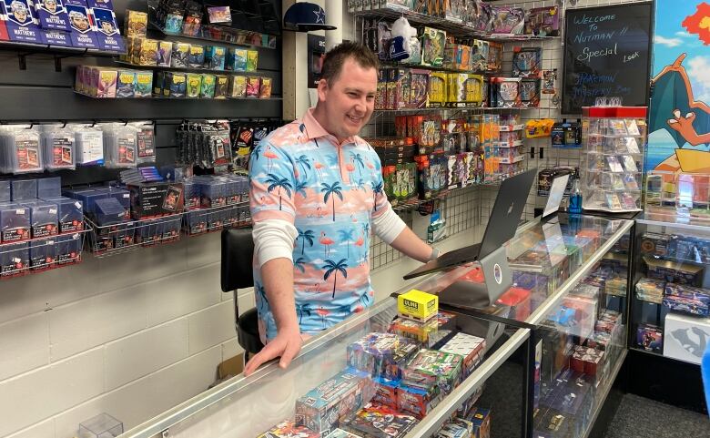 Tanner Piper is standing behind the counter of his card selling shop with cards stacked behind him on shelves