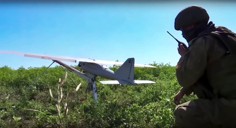 A soldier crouches behind a drone in a field