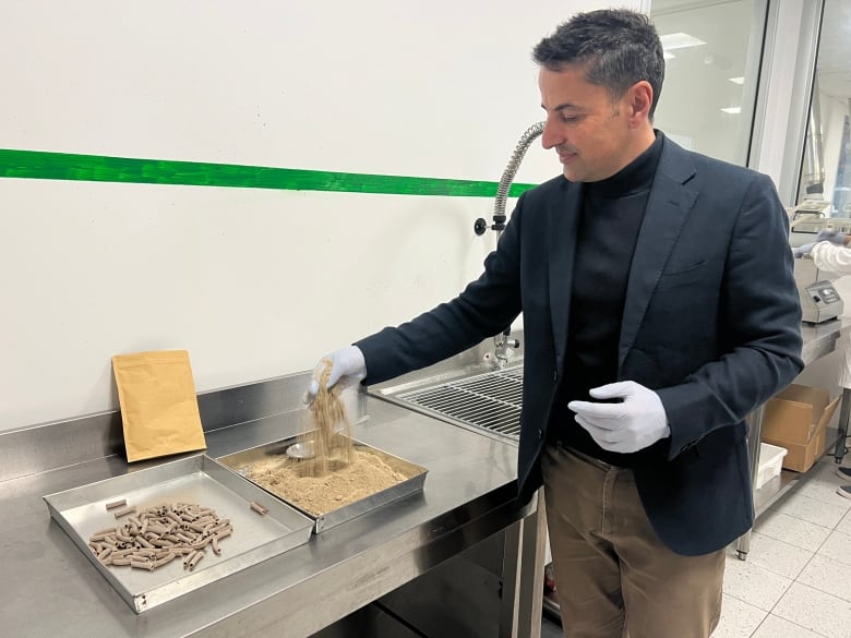 A man pours powder out of his hand into a metal tray while wearing blue gloves.