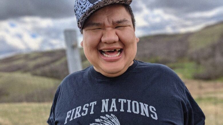 A man smiles into a camera with a shirt that reads First Nations. 