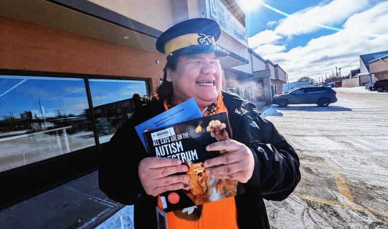 A man is looking right with a police hat on smiling with books in his hands. 