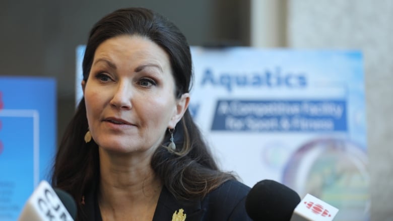 A woman in a black blazer stands in front of a posterboard with the word Aquatics on it. 