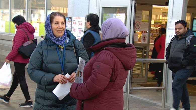 Two women hold flyers standing outside a grocery store