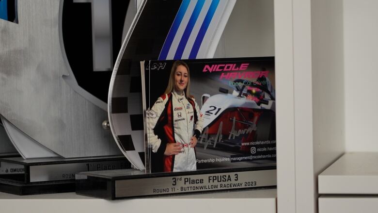 A photo of Nicole Havrda in front of her car, set in front of trophies from her racing career. 