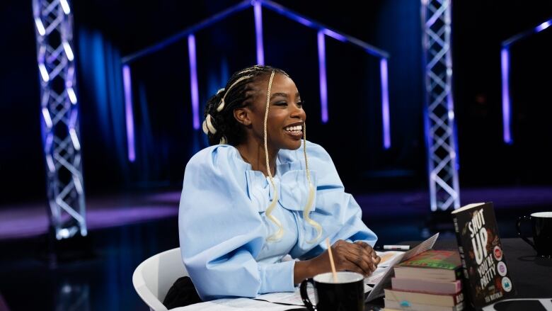 A Black woman wearing a blue outfit smiles while sitting at a round table. 