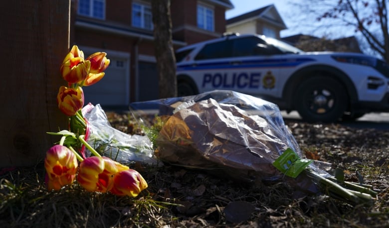 Bundles of flowers on a suburban lawn at the end of winter. A police car is in the background.