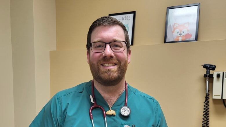 a man in blue scrubs, wearing glasses and has a stethoscope around his neck. 