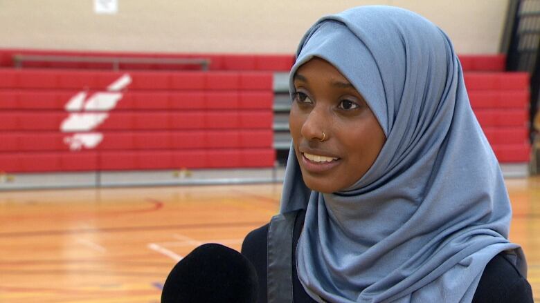 A woman wearing a blue headwrap stands in a gymnasium.