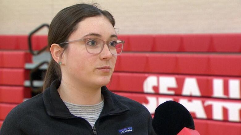 A woman wearing glasses and a pony tail stands in front of a set of red bleachers.