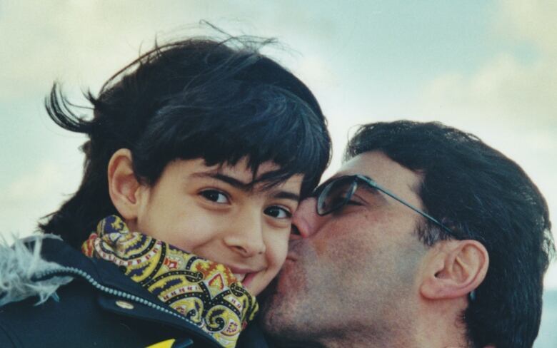 A man holds a young girl up in the air, kissing her on the cheek as she smiles at the camera.