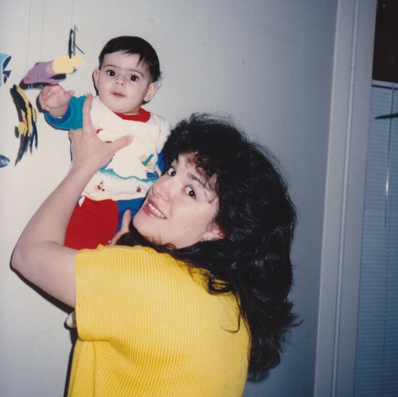 A woman holds a baby up next to a mobile.