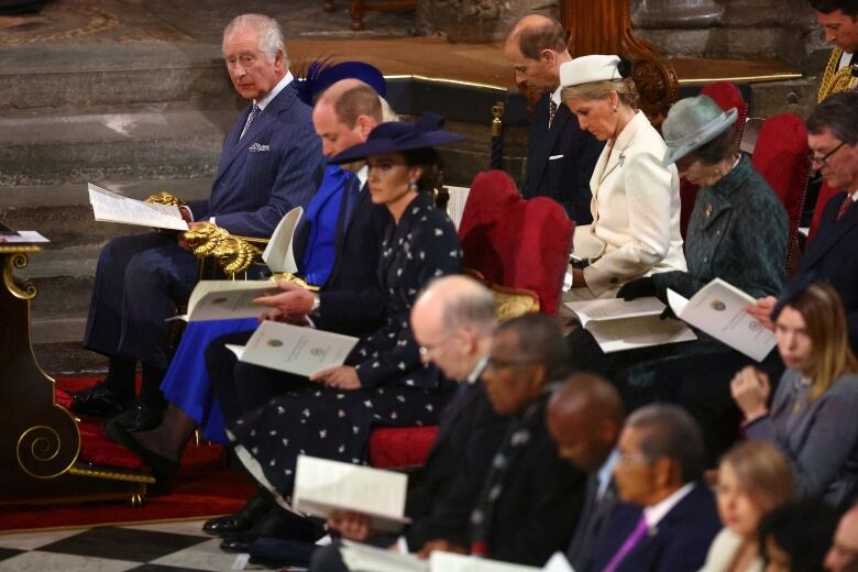 People holding programs sit on chairs in a large church.